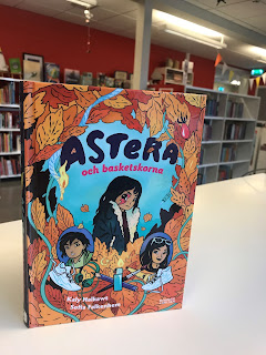 Bild av boken som står på en disk i ett bibliotek. På Bokens framsida syns Astera i mitten och hennes bror och mamma finns också med.