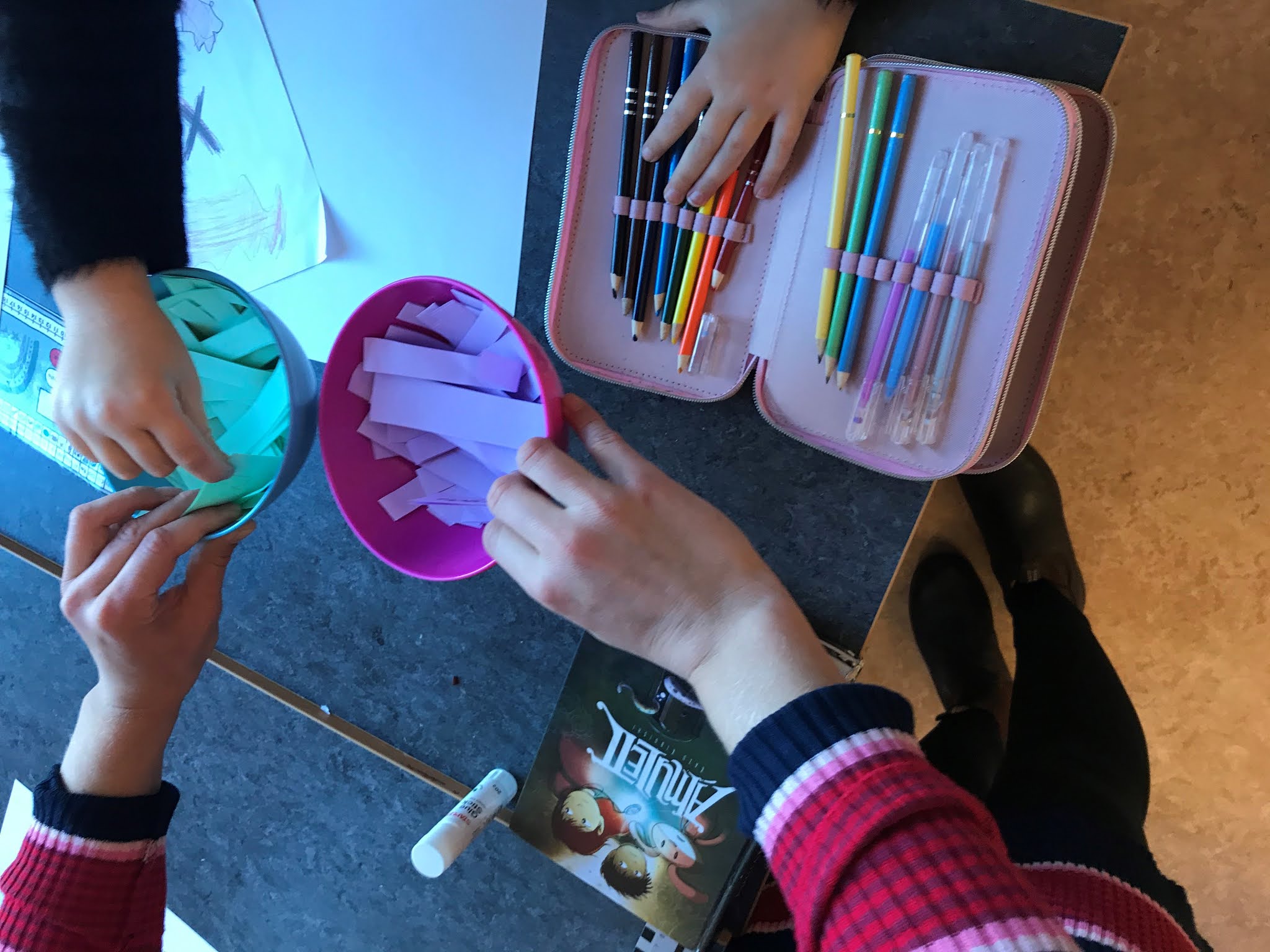 barnhänder som tar färgpennor och lappar i olika skålar